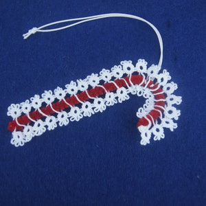 May include: White crocheted candy cane ornament with a red and white striped center. The ornament has a white string loop for hanging.