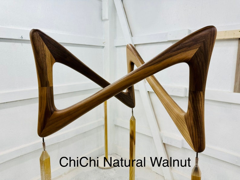 May include: A pair of wooden wall sculptures in the shape of a triangle with a natural walnut finish. The sculptures are attached to a metal rod with a gold tassel hanging from each.