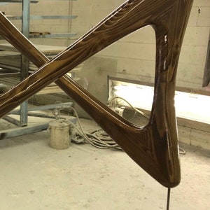 May include: Dark brown wooden sculpture with a triangular shape and a smooth, glossy finish. The sculpture is attached to a wooden base with a metal screw.