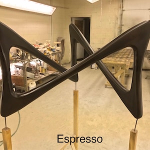 May include: A pair of dark brown wooden wall sculptures in the shape of a triangle with rounded edges. The sculptures are mounted on wooden poles and are arranged in a criss-cross pattern. The text "Espresso" is visible at the bottom of the image.
