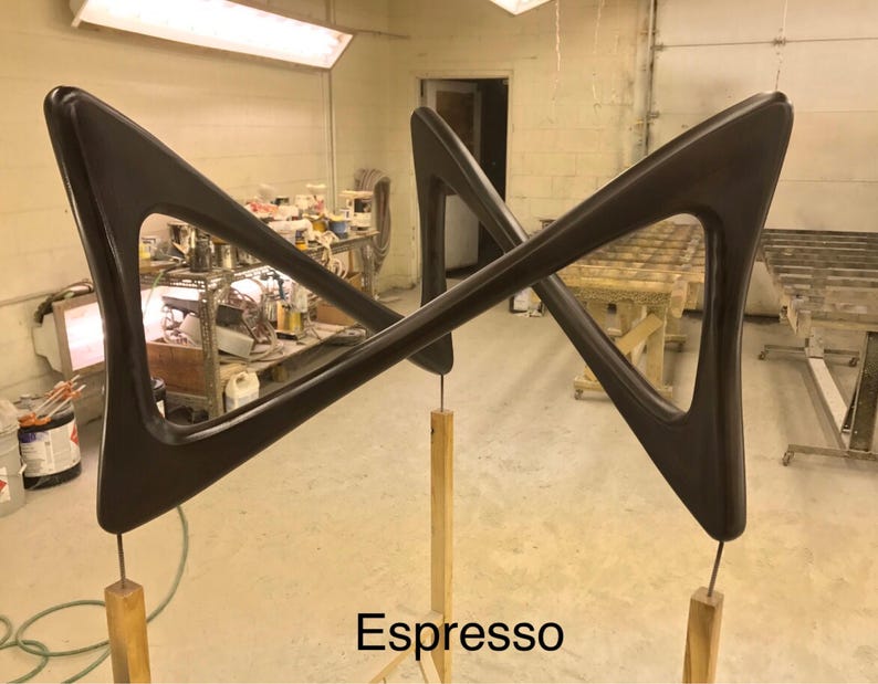 May include: A pair of dark brown wooden wall sculptures in the shape of a triangle with rounded edges. The sculptures are mounted on wooden poles and are arranged in a criss-cross pattern. The text "Espresso" is visible at the bottom of the image.