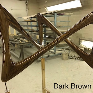 May include: Two dark brown wooden pieces shaped like triangles, joined together in a criss-cross pattern. The wood has a glossy finish and a visible grain pattern. The pieces are mounted on wooden posts. "Dark Brown" is written in white text below the pieces.