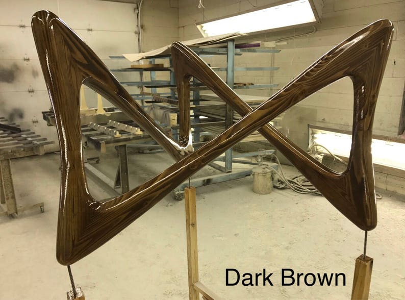 May include: Two dark brown wooden pieces shaped like triangles, joined together in a criss-cross pattern. The wood has a glossy finish and a visible grain pattern. The pieces are mounted on wooden posts. "Dark Brown" is written in white text below the pieces.