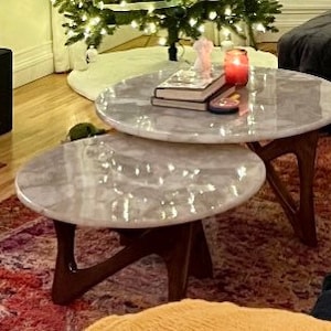 May include: Two round nesting coffee tables with white marble tops and dark brown wooden legs. The tables are on a patterned rug.