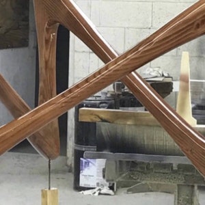 May include: A wooden sculpture with a medium brown finish. The sculpture is made of two pieces of wood that are crossed over each other. The sculpture is standing on a wooden base.