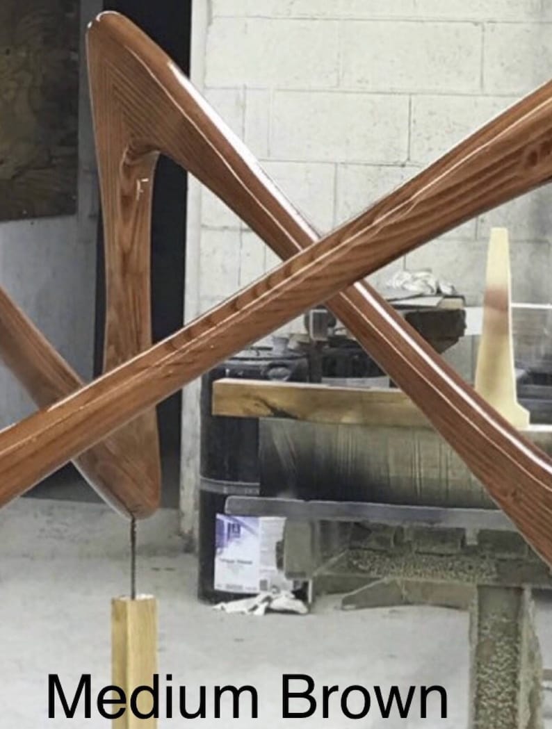 May include: A wooden sculpture with a medium brown finish. The sculpture is made of two pieces of wood that are crossed over each other. The sculpture is standing on a wooden base.