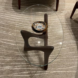 May include: A glass oval-shaped coffee table with a dark wood base and a decorative plate on top.