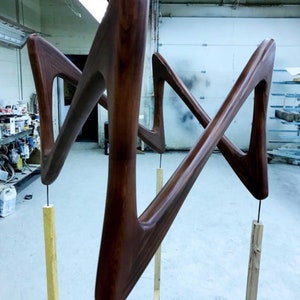 May include: Two wooden sculptures in the shape of a stylized 'M' are mounted on wooden poles. The sculptures are a deep brown color and have a smooth, polished finish. The text "Deep Cabernet" is visible at the bottom of the image.