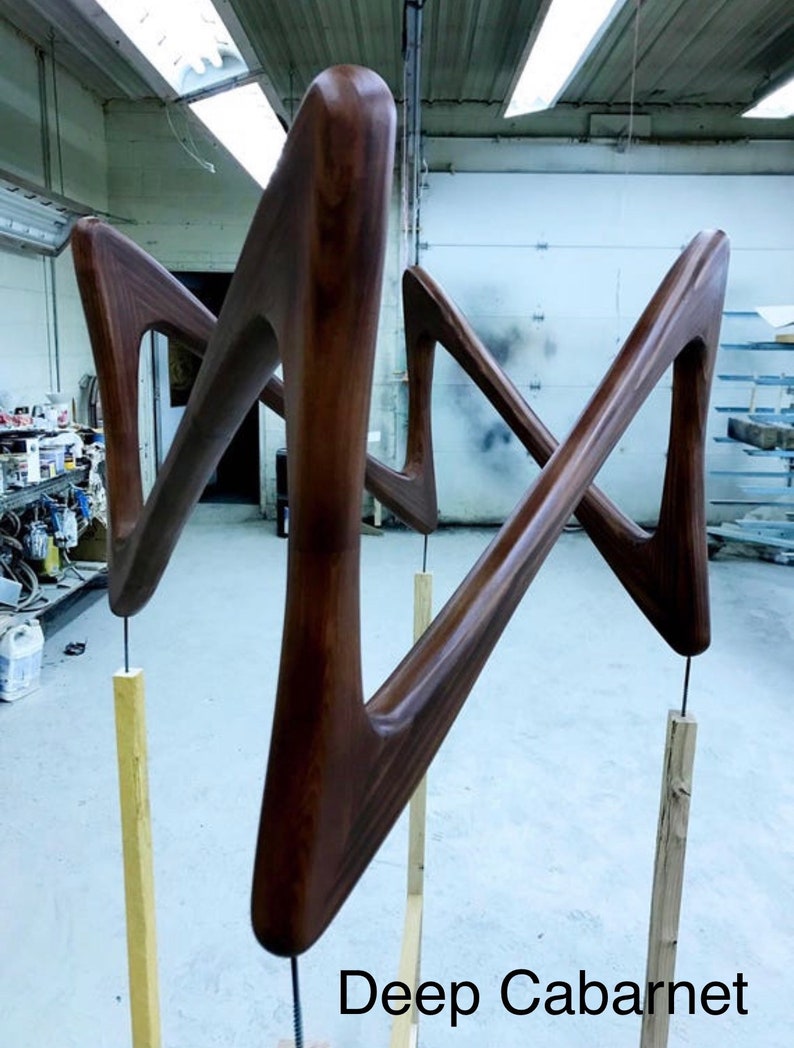 May include: Two wooden sculptures in the shape of a stylized 'M' are mounted on wooden poles. The sculptures are a deep brown color and have a smooth, polished finish. The text "Deep Cabernet" is visible at the bottom of the image.