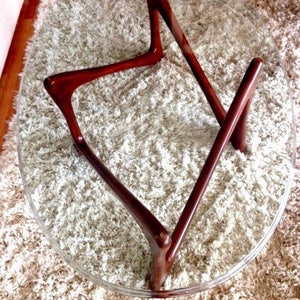 May include: A round glass table top with a unique, mid-century modern wooden base. The base is made of dark brown wood and has a geometric design.