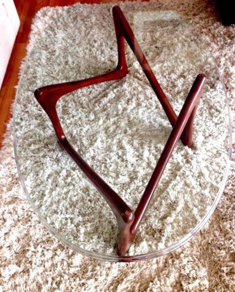May include: A round glass table top with a unique, mid-century modern wooden base. The base is made of dark brown wood and has a geometric design.
