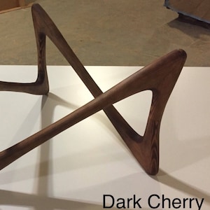 May include: Dark cherry wood coffee table base with a unique, modern design. The base is made of four pieces of wood that are joined together in a criss-cross pattern.