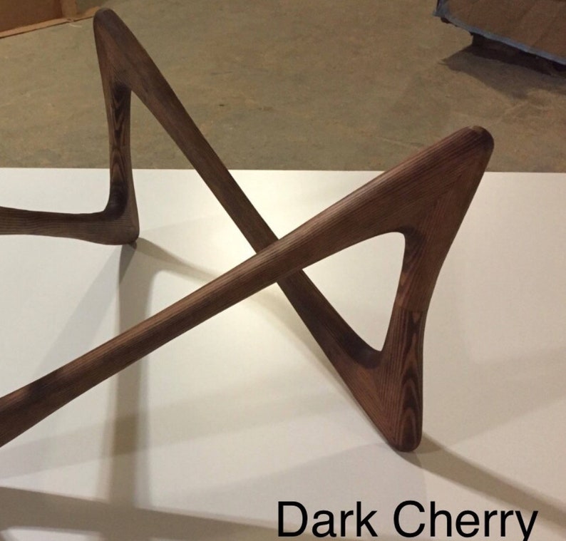 May include: Dark cherry wood coffee table base with a unique, modern design. The base is made of four pieces of wood that are joined together in a criss-cross pattern.