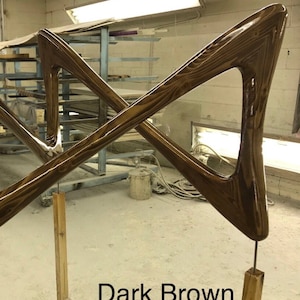 May include: Dark brown wooden sculpture with a geometric design. The sculpture is made of two pieces of wood that are crossed at the center. The sculpture is mounted on a wooden stand.