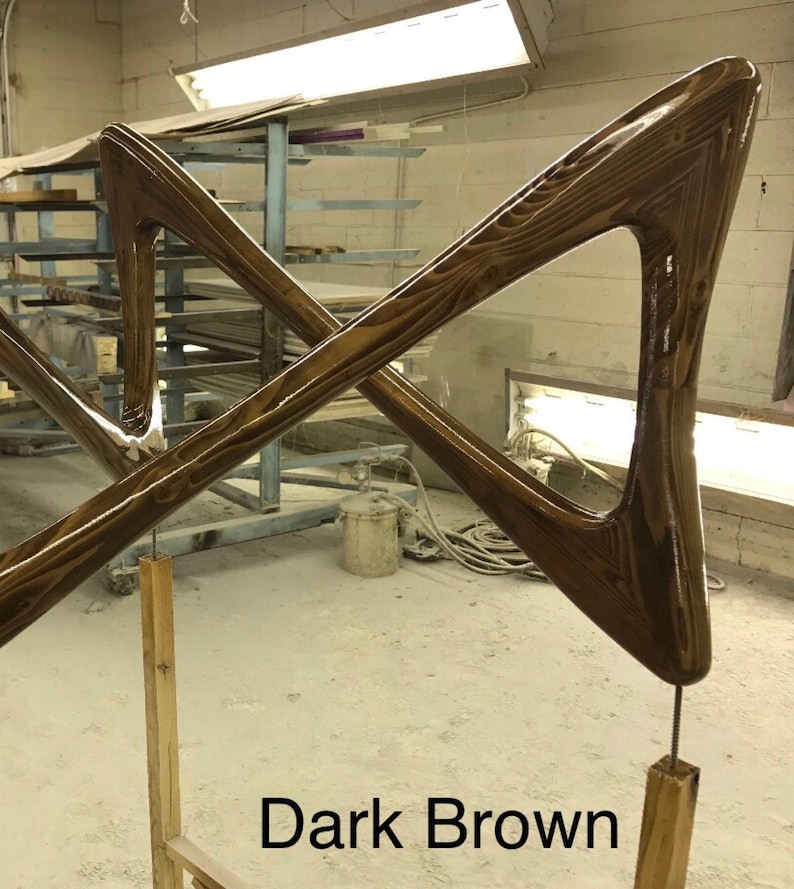 May include: Dark brown wooden sculpture with a geometric design. The sculpture is made of two pieces of wood that are crossed at the center. The sculpture is mounted on a wooden stand.