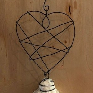 May include: A white fabric tassel hangs from a black wire heart-shaped ornament. The heart is made of wire and has a delicate, intricate design.