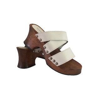 May include: White leather sandals with two straps and a wooden platform heel. The heel is brown and has a textured surface.