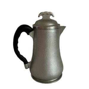 May include: A silver pitcher with a textured surface and a black handle. The pitcher has a lid with a decorative design.