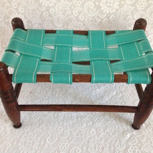 May include: A wooden footstool with a woven turquoise and white fabric seat.