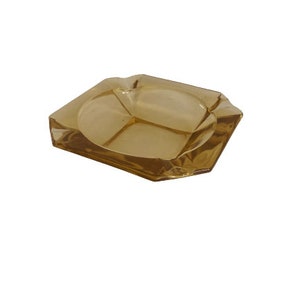 May include: A square, amber glass ashtray with a divided interior. The ashtray has a slightly textured surface.