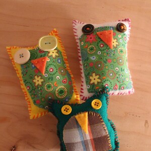 May include: Three handmade felt owl ornaments with different patterns and colors. The owls have yellow, orange, and green accents.