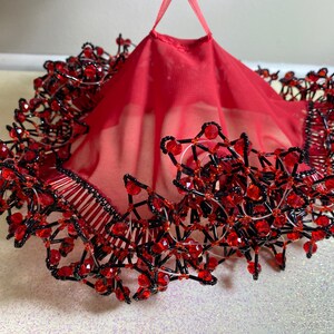 May include: A red sheer fabric skirt with a black and red beaded trim. The beads are arranged in a geometric pattern.