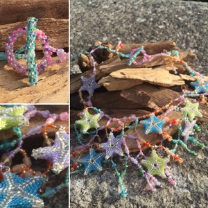 Peut inclure: Un collier de perles avec un motif en &eacute;toile. Le collier est fait de perles iris&eacute;es dans des tons de bleu, vert, rose et violet. Le collier est enfil&eacute; sur un fil d'argent et poss&egrave;de un fermoir &agrave; mousqueton.