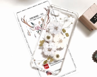 May include: A clear phone case featuring pressed white flowers, arranged in a cluster in the centre. The case has a white background and the text "AINOHANA - YYL" is printed on it, along with the Etsy logo and a website address.