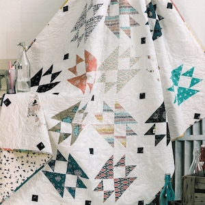 May include: A white quilt with a geometric pattern of black, teal, orange, and yellow triangles. The quilt is folded and draped over a wooden crate.