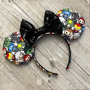 May include: Black sequined Minnie Mouse ears with a fabric bow and a white background featuring a pattern of various Marvel characters.
