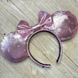 Peut inclure: Oreilles de souris Minnie en velours rose avec une finition scintillante et un grand nœud.