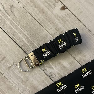 May include: Black and white fabric keychain with the text "EW, DAVID" repeated on it. The keychain has a gold metal ring.