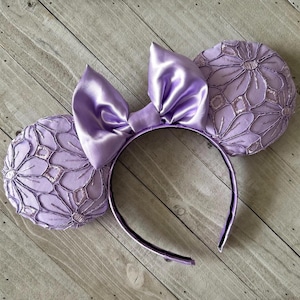 May include: Purple satin bow headband with two lavender lace ears. The headband is decorated with a large satin bow and the ears are made of delicate lace.
