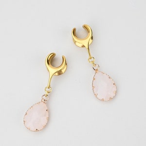Monturas para orejas en forma de media luna dorada con lágrima de cuarzo rosa. Tamaños disponibles desde 2 g hasta 30 mm.