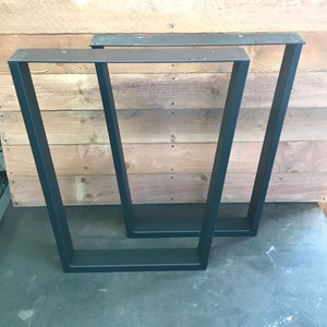 May include: Two black metal table legs, one stacked on top of the other. The legs are rectangular in shape and have a simple, modern design.