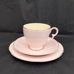 Puede incluir: Un juego de taza y platillo de té rosa con ribete dorado. La taza de té tiene un interior de color crema.