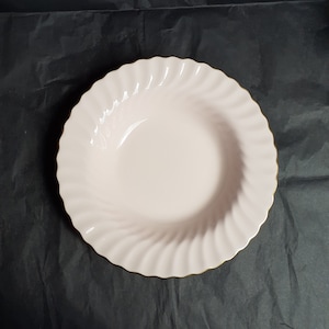 May include: A pink porcelain soup bowl with a gold rim and a wavy design.