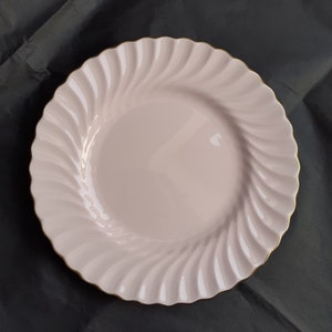 May include: A pink ceramic dinner plate with a swirl design and a gold rim.