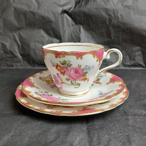 Puede incluir: Un juego de taza y platillo de té vintage con un patrón floral en tonos de rosa, amarillo y verde. El juego presenta un delicado borde dorado y un diseño estampado en rosa y blanco.