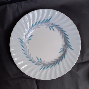 May include: A white ceramic plate with a scalloped edge and a blue and grey floral design.