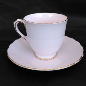 May include: A pink teacup and saucer set with a gold trim. The cup and saucer are both made of porcelain.