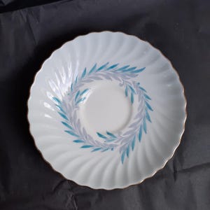 May include: White saucer with a gold rim and a blue and grey leaf design.