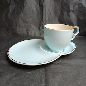 Puede incluir: Juego de taza y platillo azul claro con ribete dorado. La taza tiene forma redondeada con asa, y el platillo es ovalado. El juego es de cerámica.