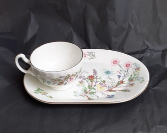 May include: A white teacup and saucer set with a floral pattern. The cup has a gold rim and the saucer has a gold edge. The floral pattern features pink, purple, blue, and yellow flowers.