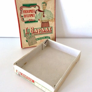 May include: Vintage cardboard box with a red and green label featuring a man adjusting his tie. The box is open, revealing its empty interior. The text on the box is in Greek.