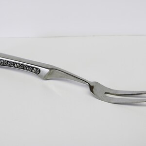 May include: A silver serving fork with a decorative, ornate handle. The fork has two tines and is designed for serving food.