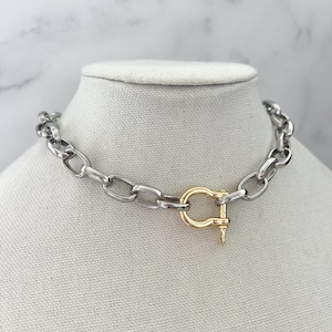 Puede incluir: Un collar de cadena plateada con un cierre dorado. El collar se exhibe sobre un busto de maniqu&iacute; blanco sobre un fondo de m&aacute;rmol. Los eslabones de la cadena son ovalados y gruesos, creando un aspecto audaz y moderno. Aproximadamente 40 cm de largo.