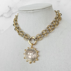 May include: A gold and silver chain necklace with a round pendant featuring a silver horse design. The pendant has a gold rim with small gold balls around the edge.
