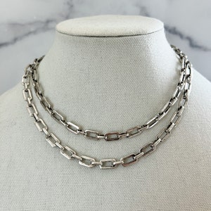 May include: Two silver chain necklaces with a box chain design. The chains are layered on a white mannequin.