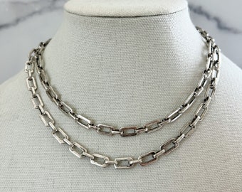 May include: Two silver chain necklaces with a box chain design. The chains are layered on a white mannequin.